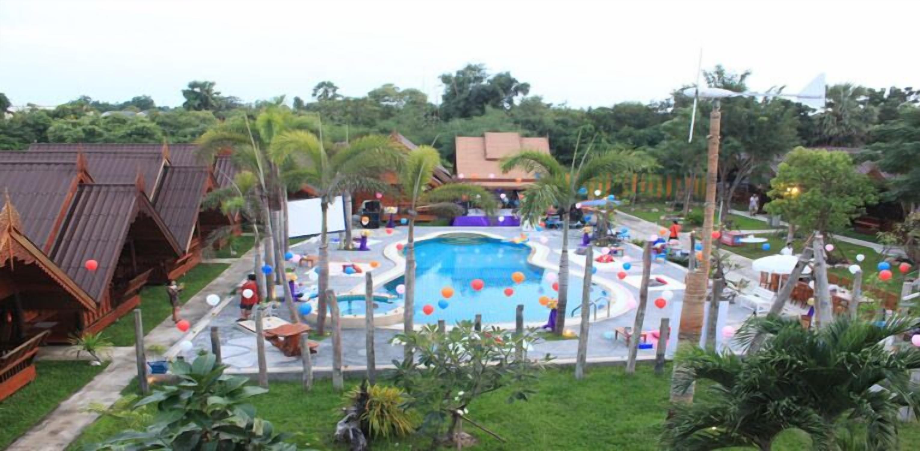 Une piscine entourée de palmiers et un bâtiment traditionnel doté d’un toit en pente.