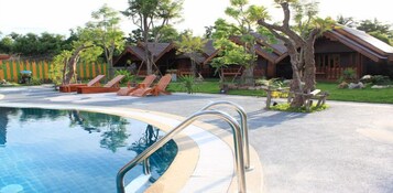 Un área de piscina con sillones de descanso y cabañas de madera.
