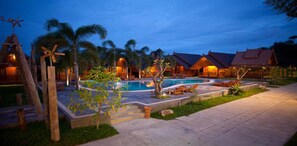 Een resort met een zwembad, palmbomen en gebouwen in traditionele stijl.