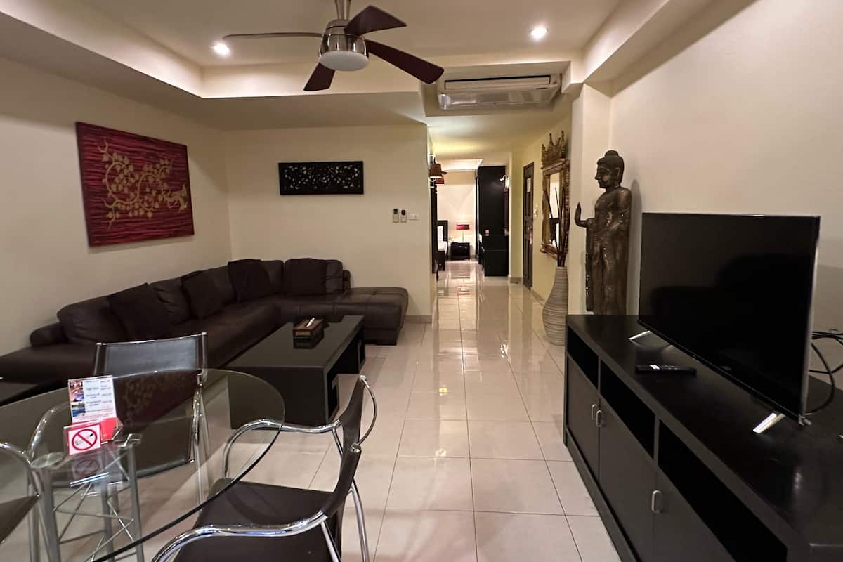 A modern living room with a sectional sofa, a glass dining table with chairs, a flat-screen TV, and a ceiling fan.