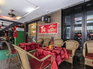 Un espace extérieur aménagé pour les repas, avec des chaises et des tables en osier recouvertes de nappes rouges. Une pancarte annonce : « Animations tous les soirs, hébergement de qualité à des prix abordables. »