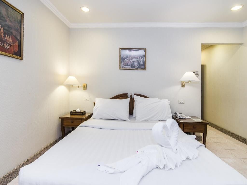A hotel room with a large bed, two bedside tables, a nightstand, a framed picture on the wall, and two wall-mounted lamps.