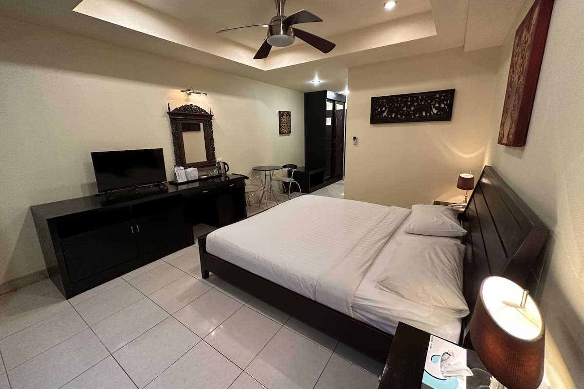 A modern hotel room with a bed, a desk, a television, a ceiling fan, and a wall-mounted artwork.