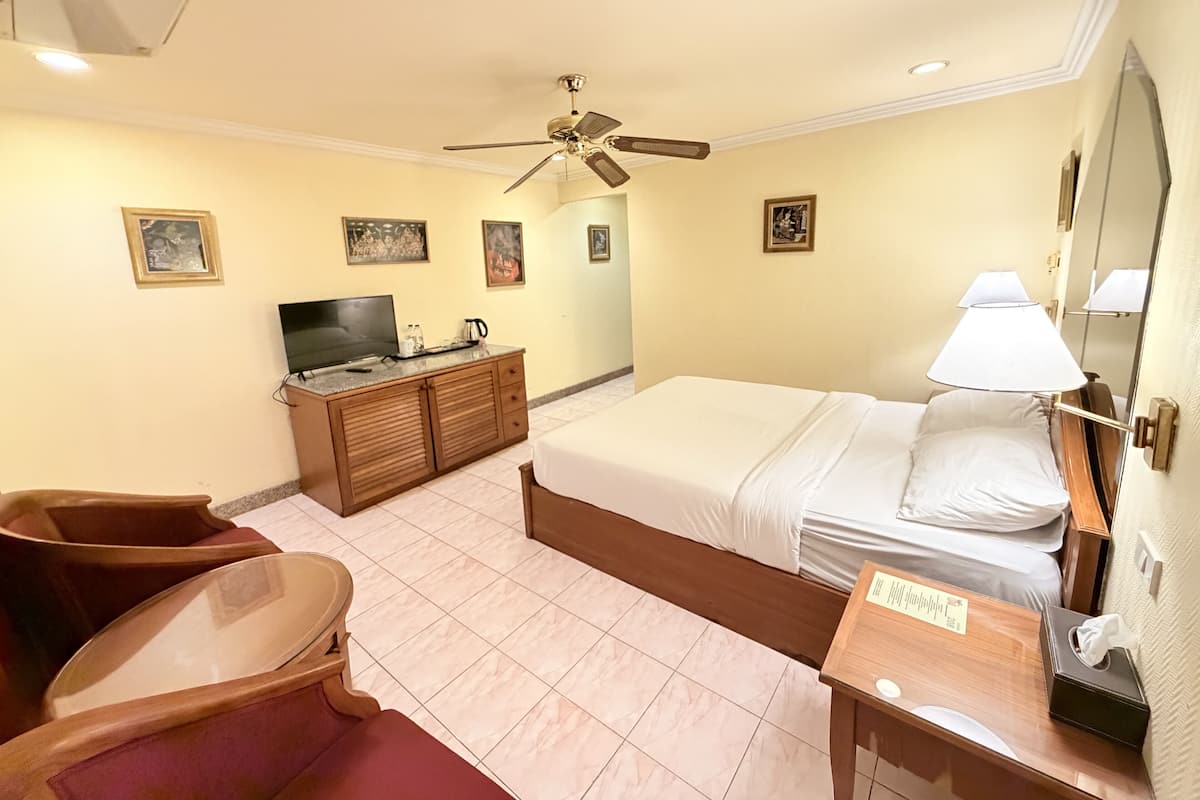 A hotel room with a bed, a desk, a chair, a television, and a ceiling fan.