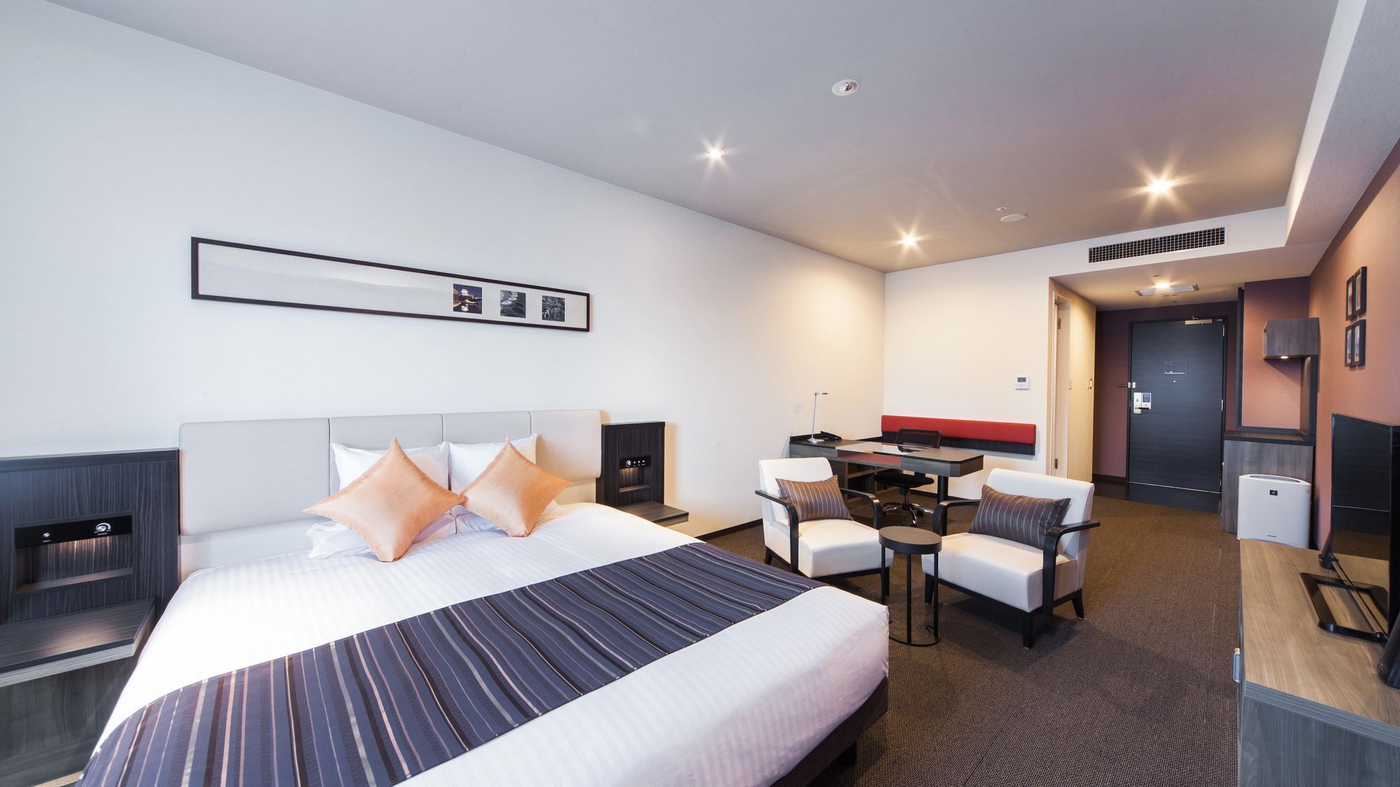 A hotel room with a bed, a desk, two chairs, a small table, and a kitchenette area.