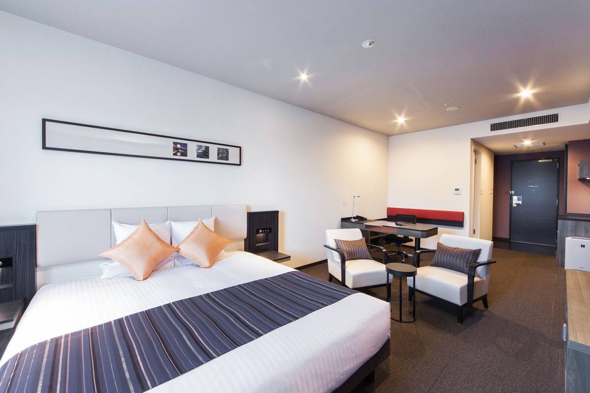 Hotellihuone, jossa on sänky, työpöytä, kaksi tuolia, pieni pöytä ja pieni keittotila.