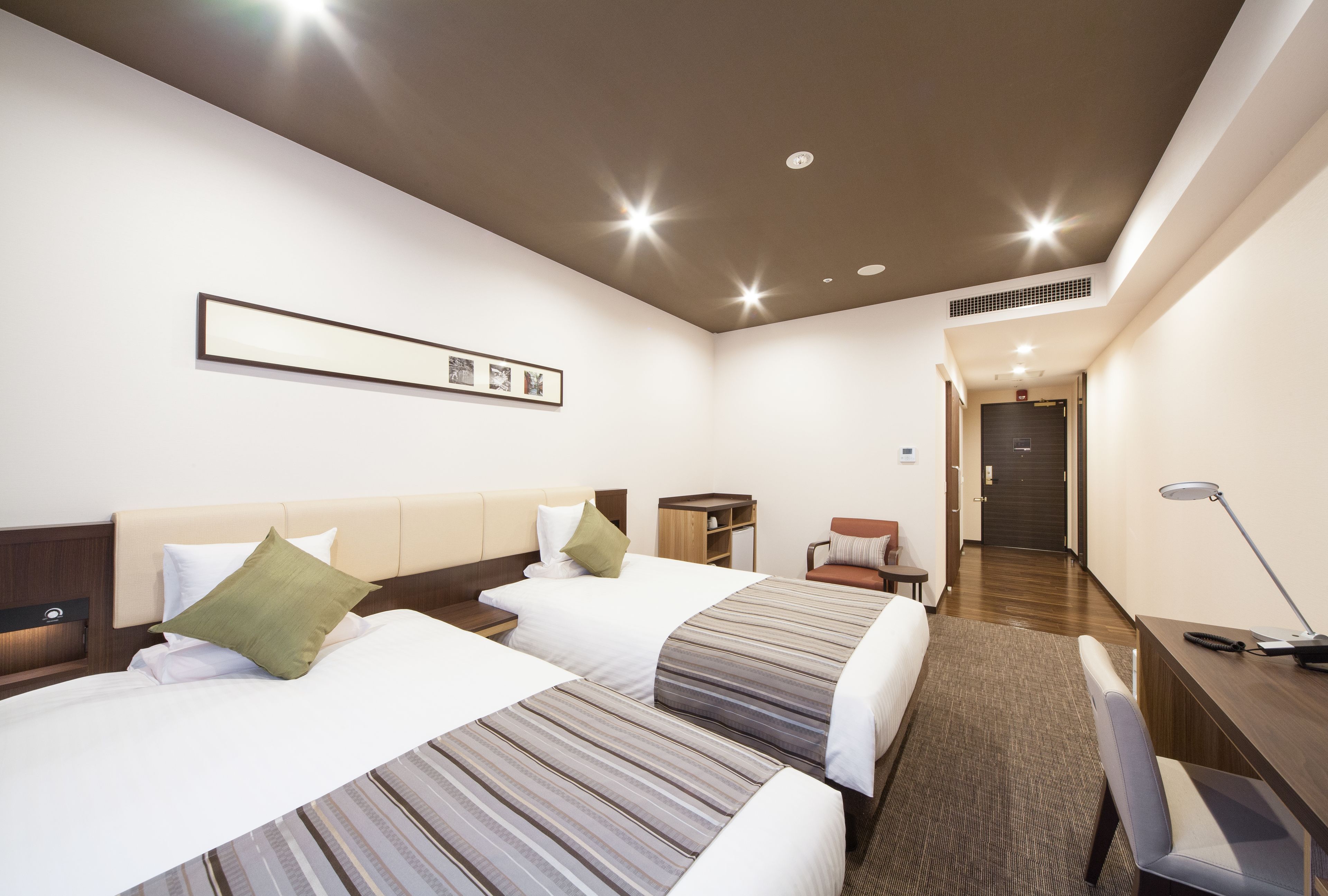 A hotel room with two beds, a desk, a chair, a lamp, and a framed picture on the wall.