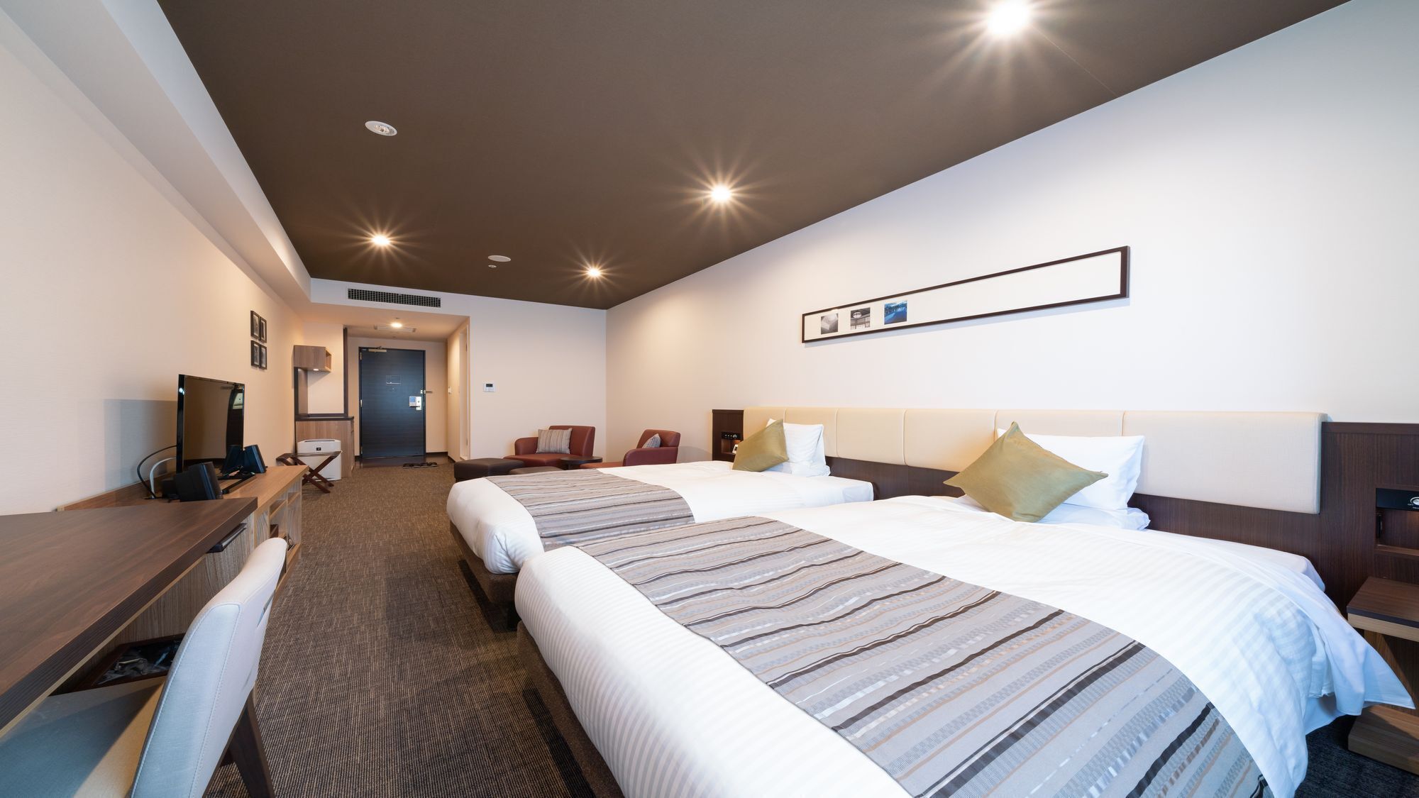A hotel room with two beds, a desk, a chair, and a TV.
