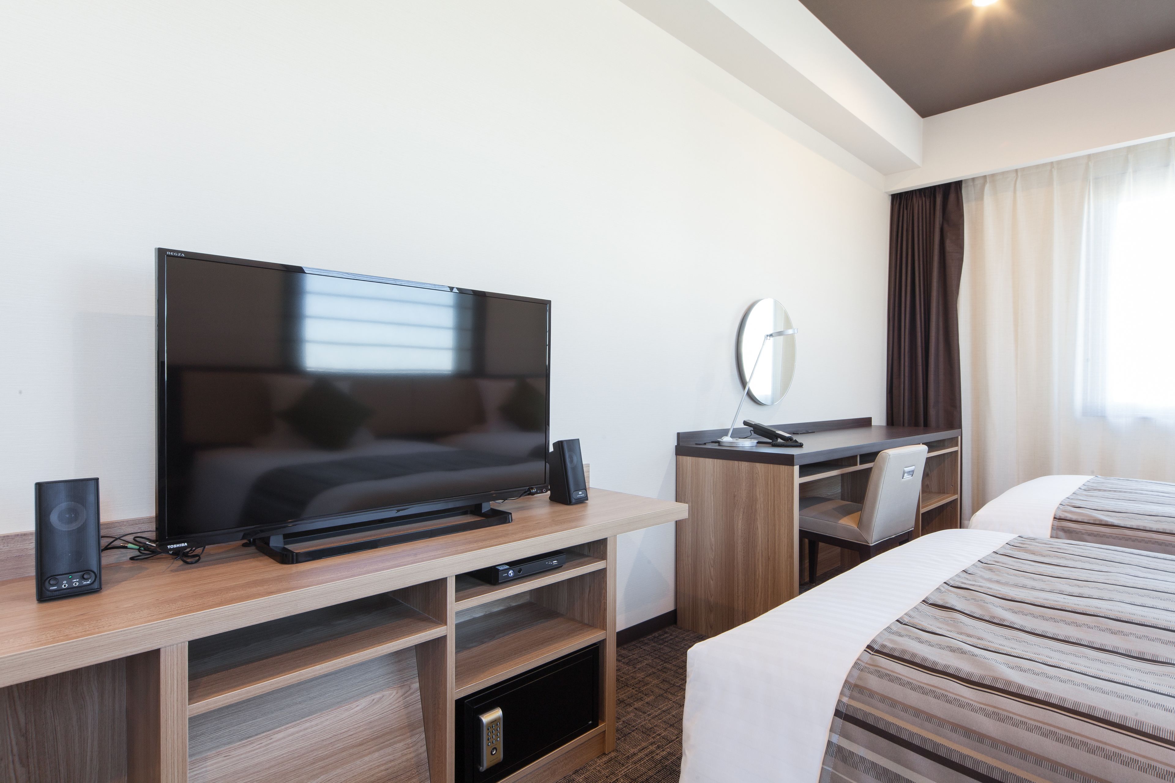 Habitación de hotel con televisor de pantalla plana, escritorio con computadora, una silla y cama con ropa de cama a rayas.