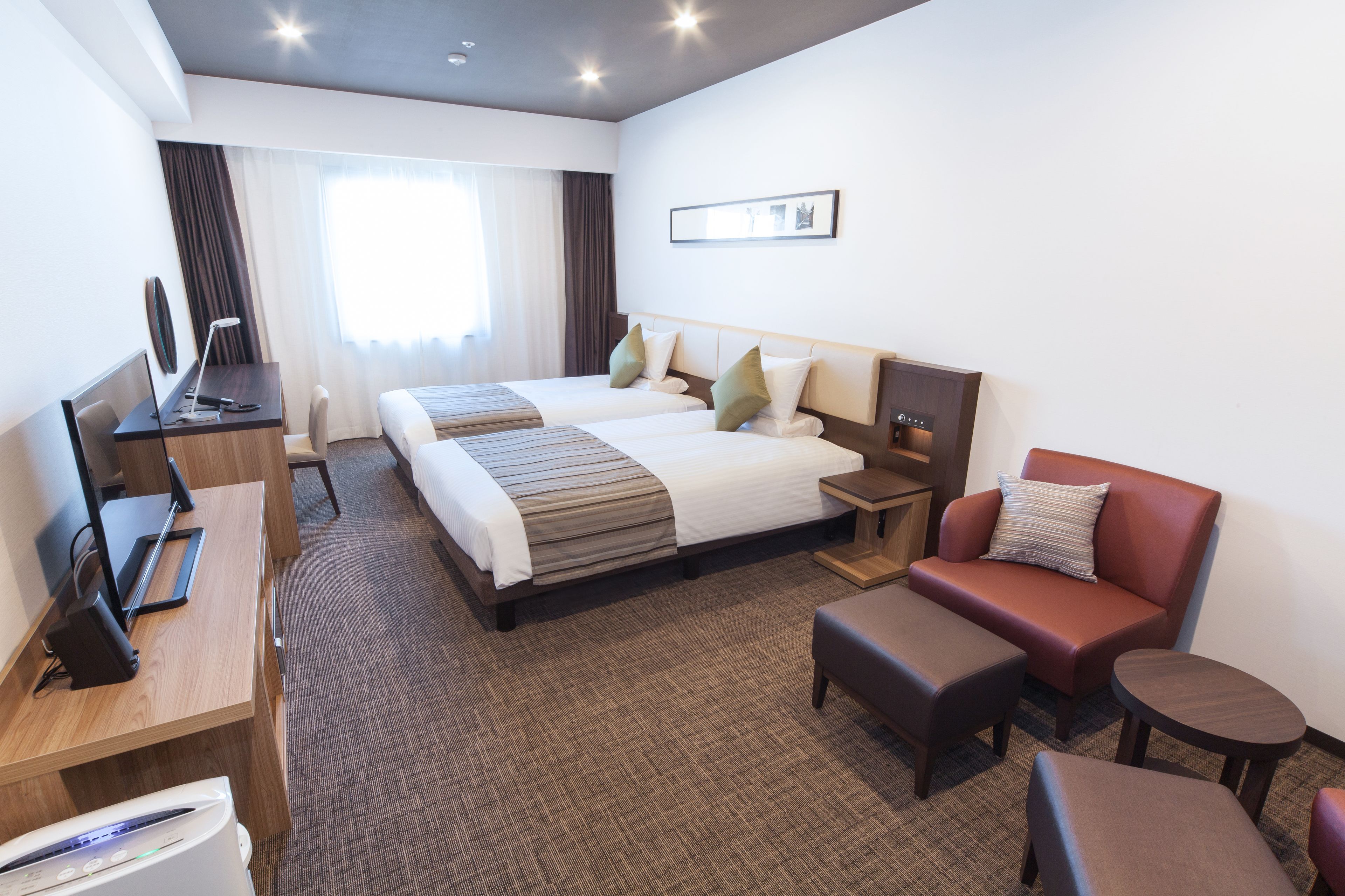 A hotel room with a bed, two bedside tables, a desk with a computer, a chair, and a small round table.