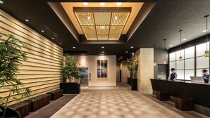 Un hall d’hôtel moderne avec un comptoir d’accueil, des plantes en pot et un plafond décoré de motifs.