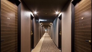 Un long couloir étroit d’hôtel, avec des portes en bois numérotées 714 et 707.