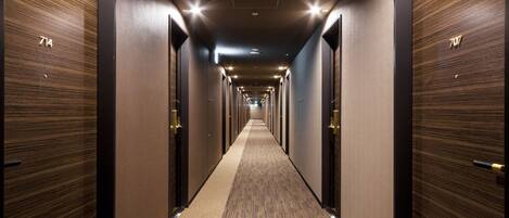 Un largo pasillo de hotel, estrecho, con puertas de madera numeradas 714 y 707.