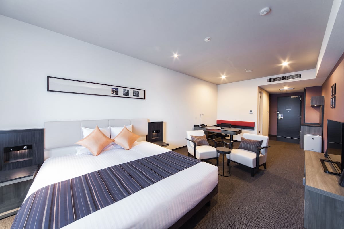 Moderni hotellihuone, jossa on suuri sänky, työpöytä ja oleskelualue.