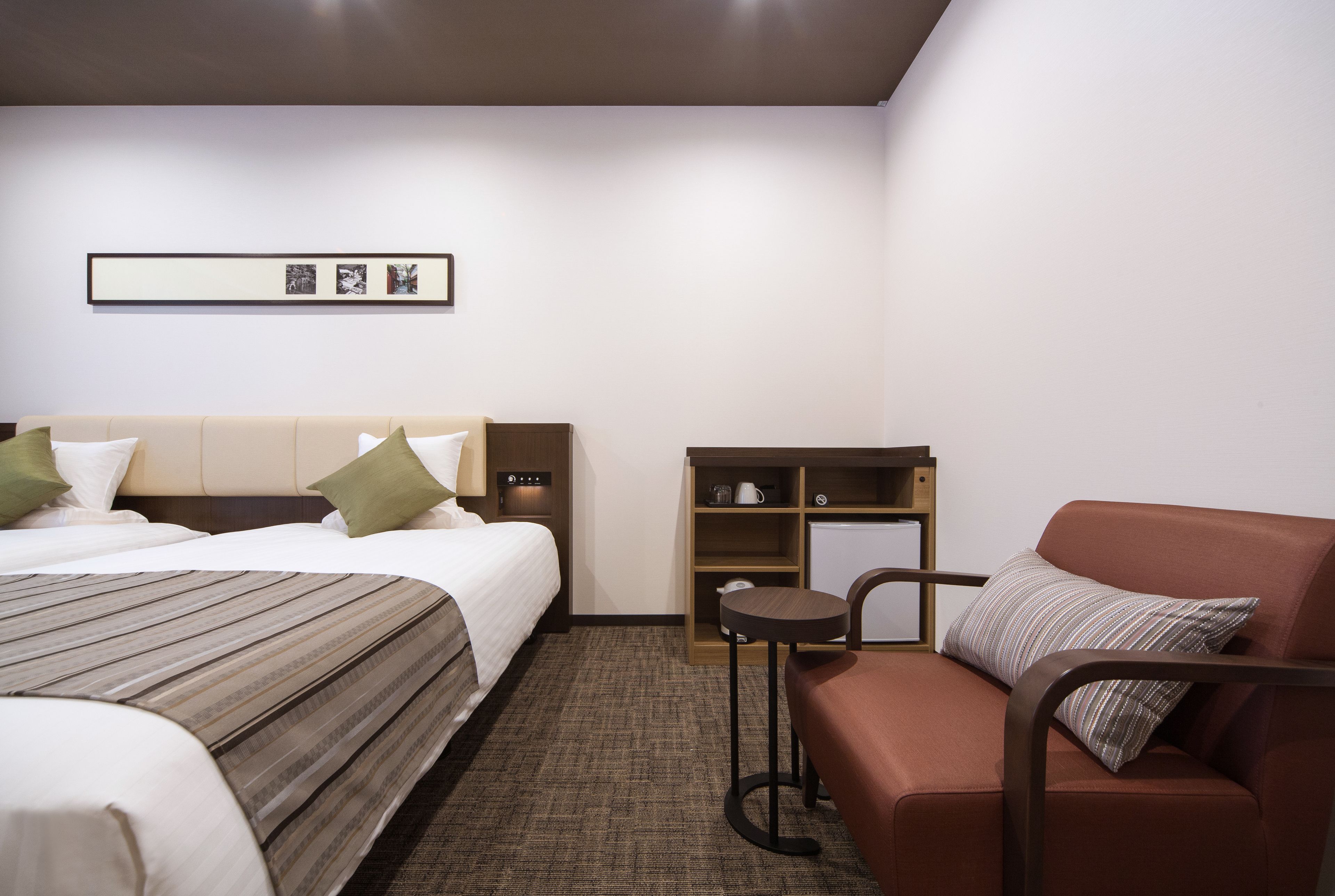 Habitació d'hotel amb llit, sofà, taula petita i prestatge amb objectes.