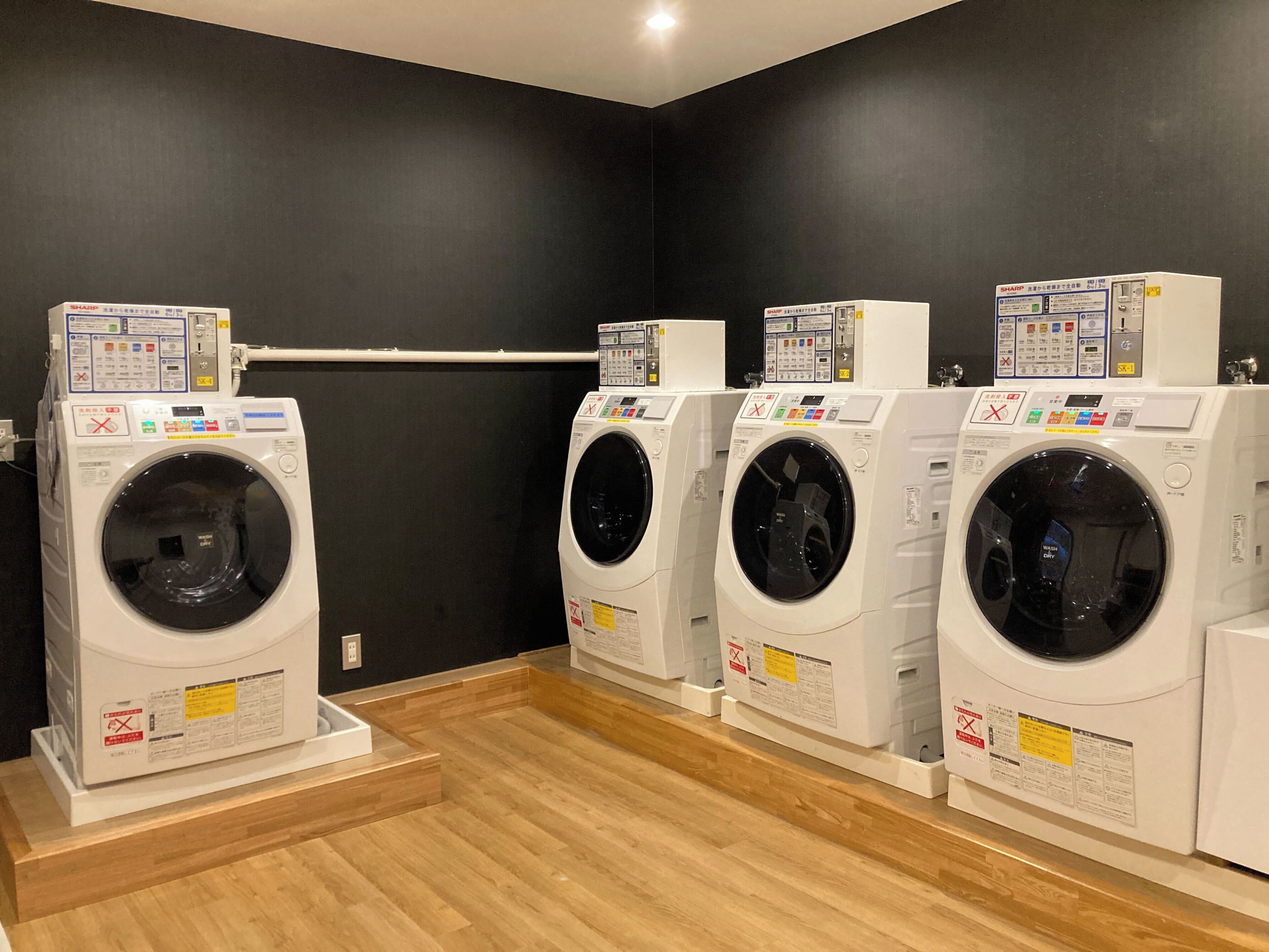 A laundry room with four washing machines lined up against a dark wall.