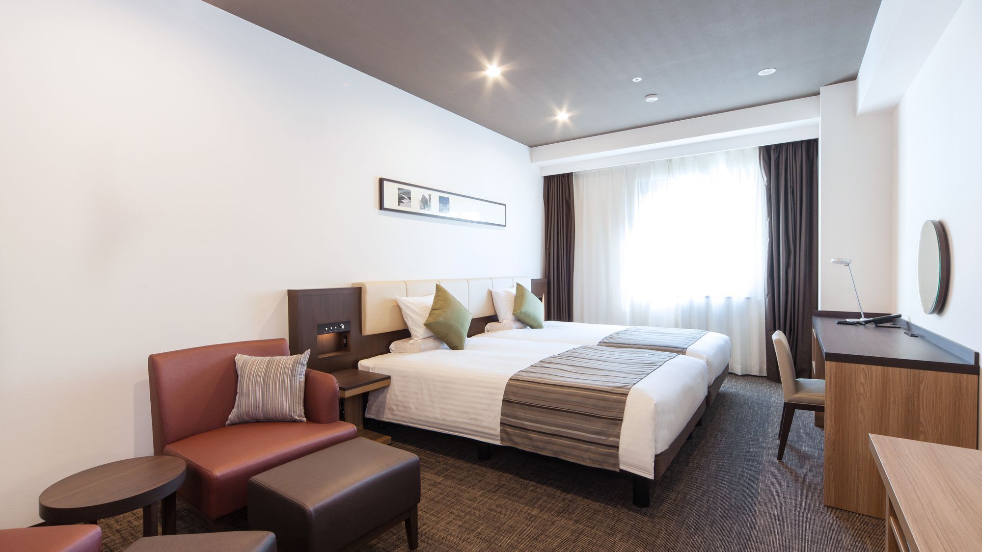 A hotel room with a bed, a desk, a chair, a sofa, and a small table.
