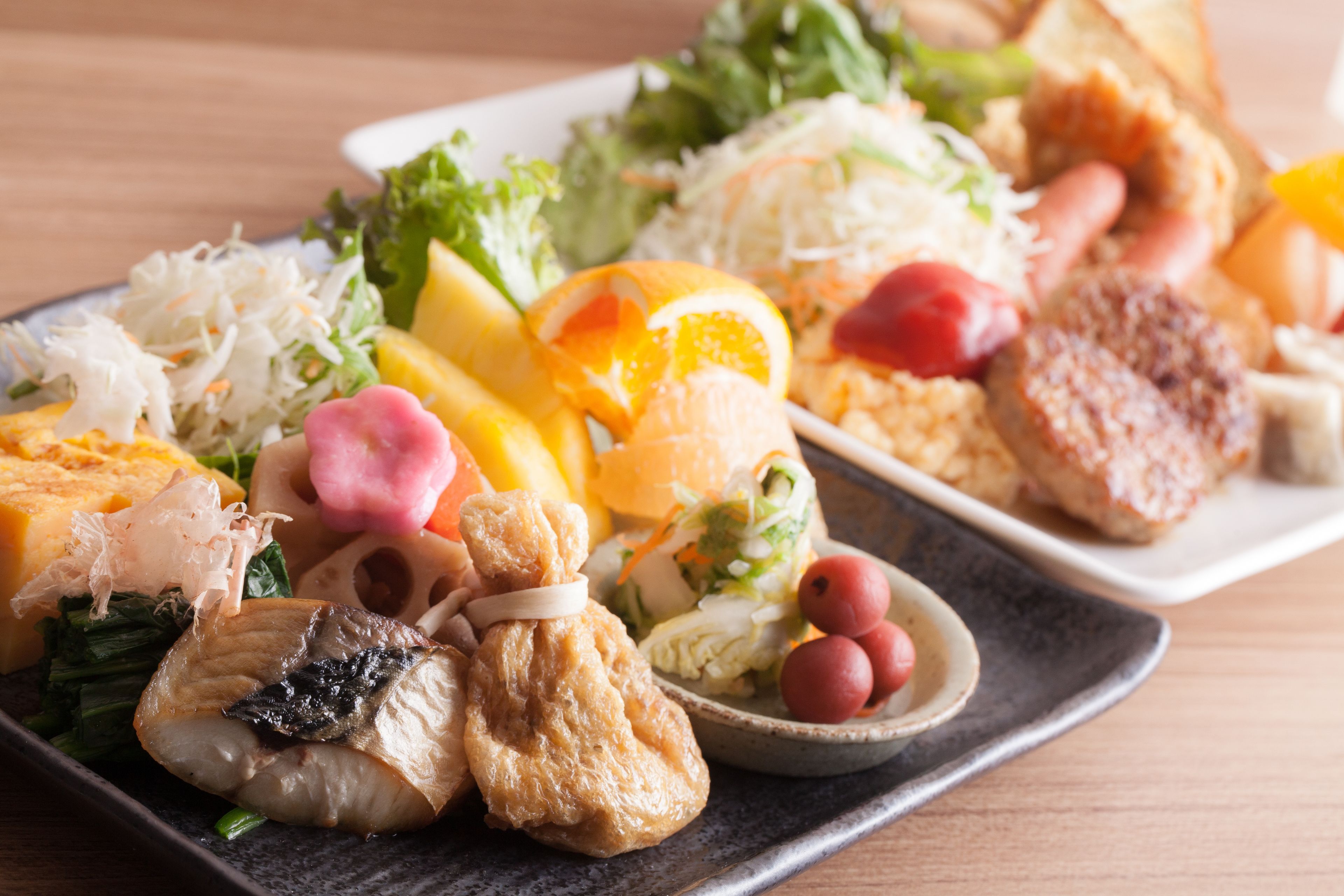 A variety of dishes including sushi, sashimi, and vegetables on a rectangular plate.