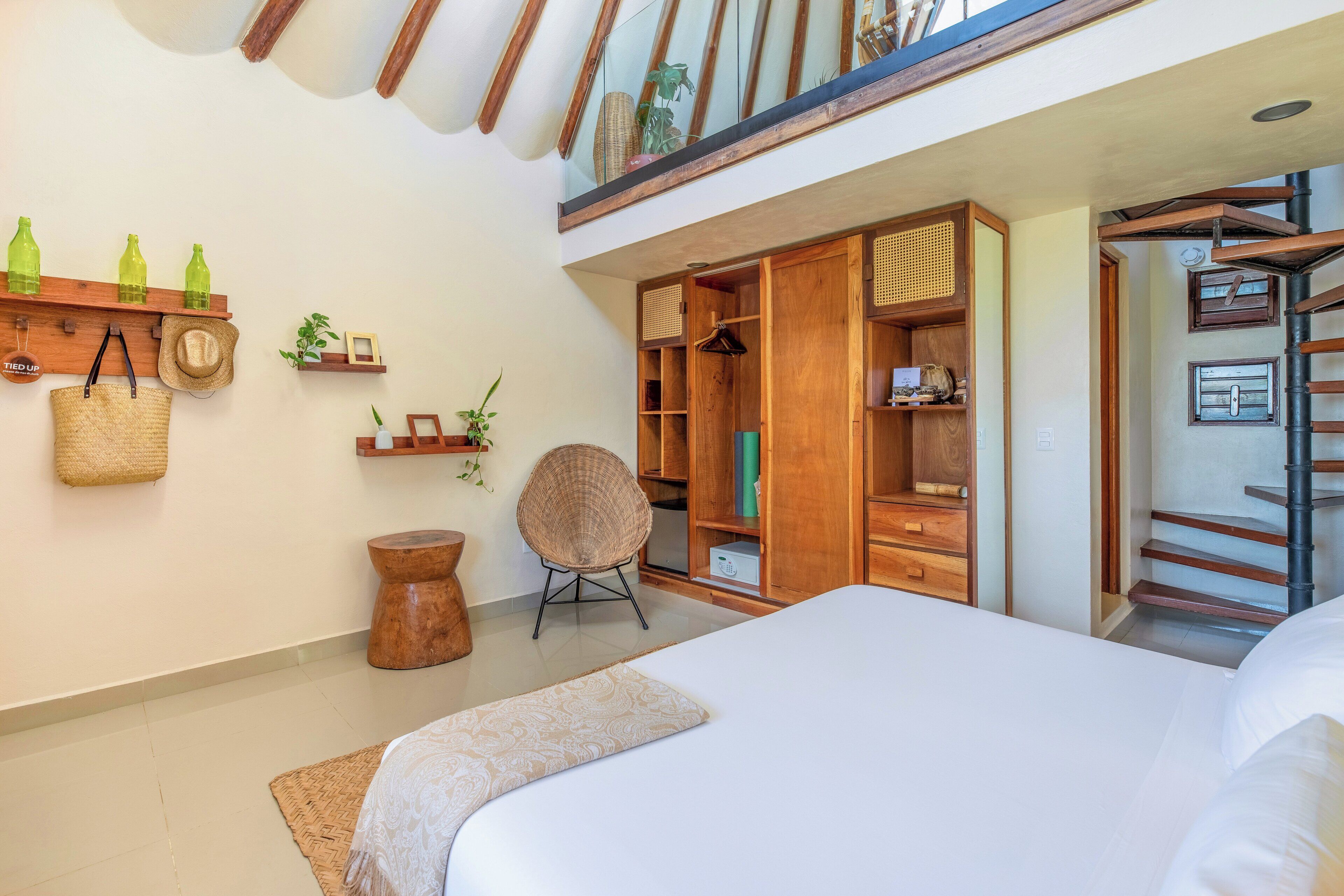 Un dormitorio con una cama grande, un armario de madera, una silla de mimbre y un taburete pequeño.