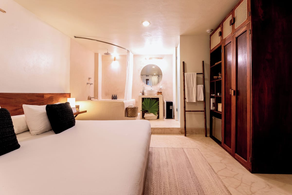 Ein Hotelzimmer mit einem großen Bett, einem Holzschrank, einem Badezimmer mit Spiegel und Waschbecken.