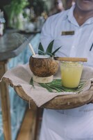 A person holding a tray with a coconut drink, a glass of yellow beverage, and a straw.