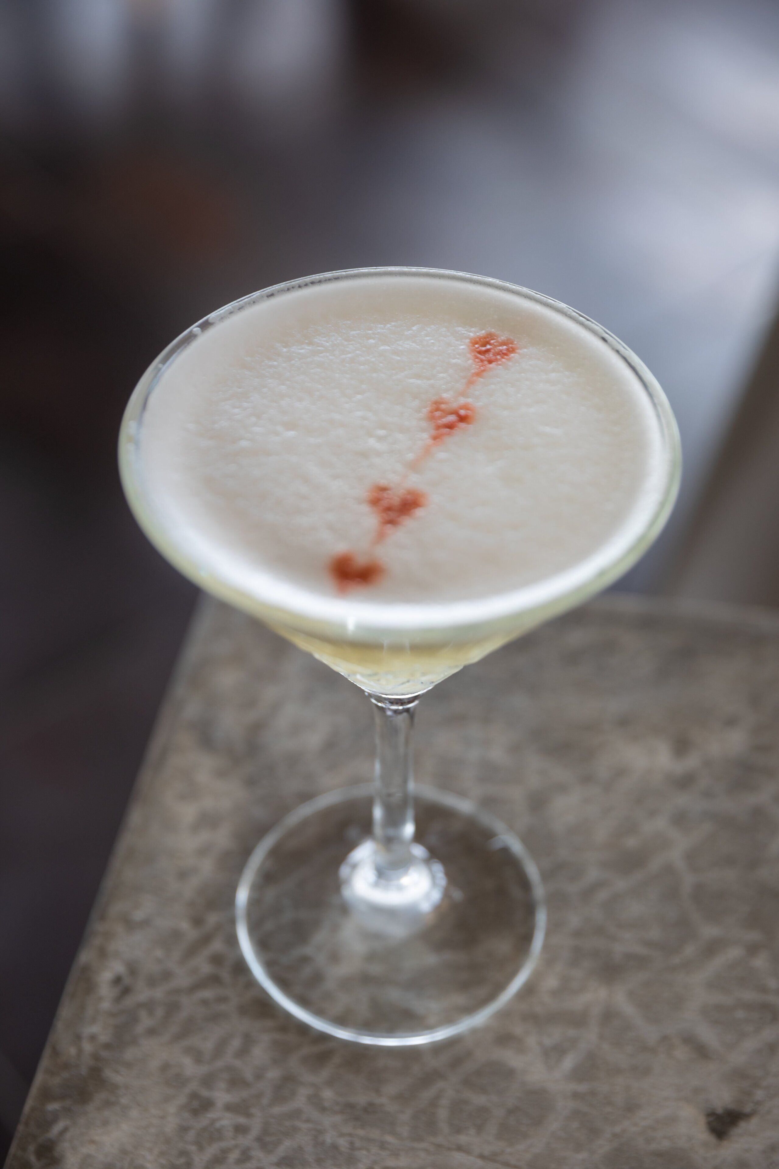 A martini glass with a frothy top on a textured surface.