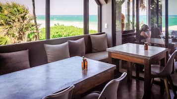Un restaurante con vista al océano, que cuenta con una mesa larga y un banco acolchado.