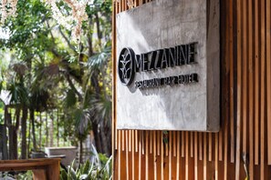 Schild für 'MEZZANINE RESTAURANT BAR HOTEL' mit Logo, vor einem Holzhintergrund mit vertikalen Lamellen.