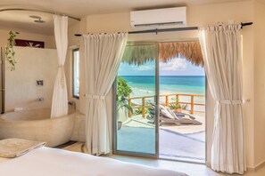 Une chambre d’hôtel dotée d’une grande baignoire, d’une porte-fenêtre coulissante donnant sur un balcon avec vue sur la plage et d’un climatiseur au plafond.