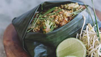A meal served in a banana leaf bowl with broccoli, rice, and bean sprouts, accompanied by lime wedges.