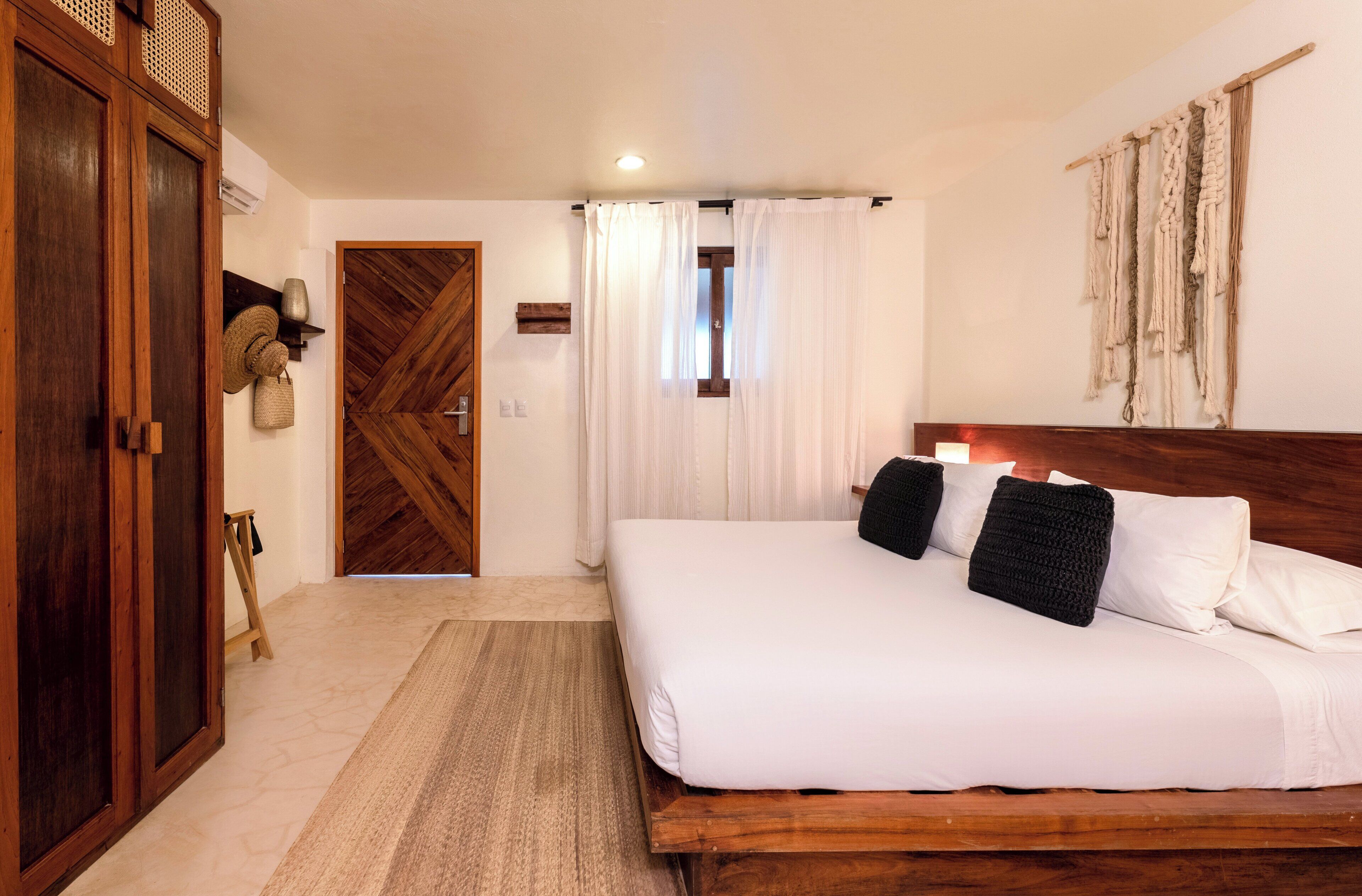 Un dormitorio con cama de madera, ropa de cama blanca, armario de madera y un tapiz tejido en la pared.