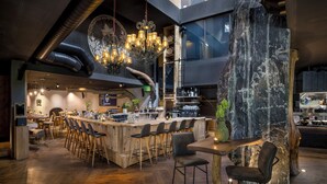 A modern bar area with a central wooden bar, multiple bar stools, and a chandelier. - mama thresl (Leogang)