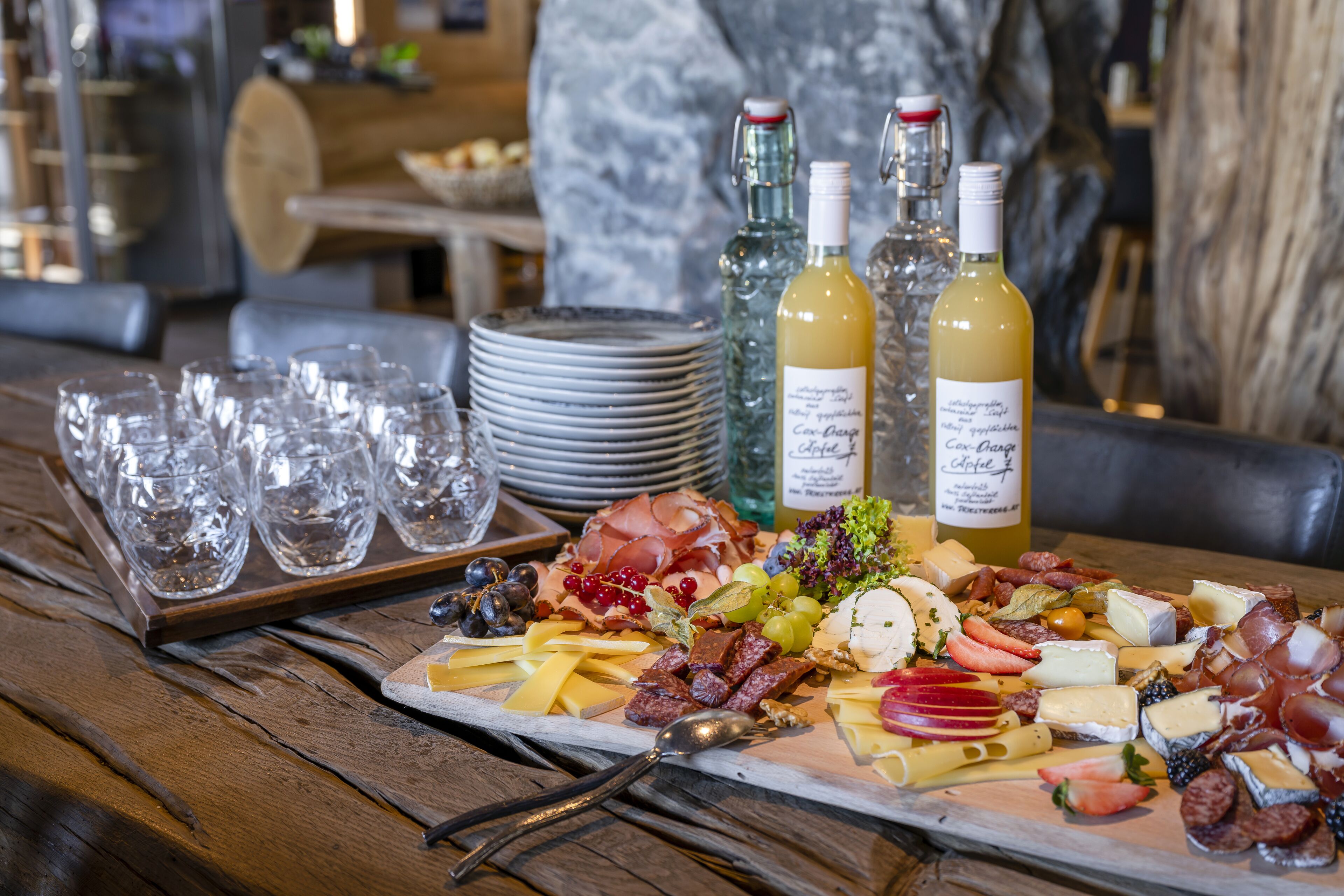 A charcuterie board with various cheeses, meats, and fruits, accompanied by wine bottles and glasses on a wooden table.