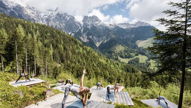 A group of people practicing yoga on wooden platforms in a mountainous area with a view of snow-capped peaks. - mama thresl (Leogang)