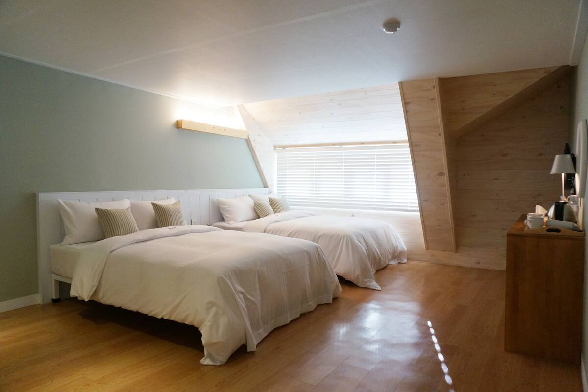 Un dormitorio con dos camas, suelo de madera, techo inclinado y una ventana con persianas.