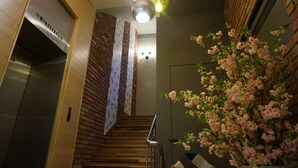 Un escalier avec des finitions en bois, un ascenseur en acier inoxydable et un luminaire fixé au mur.