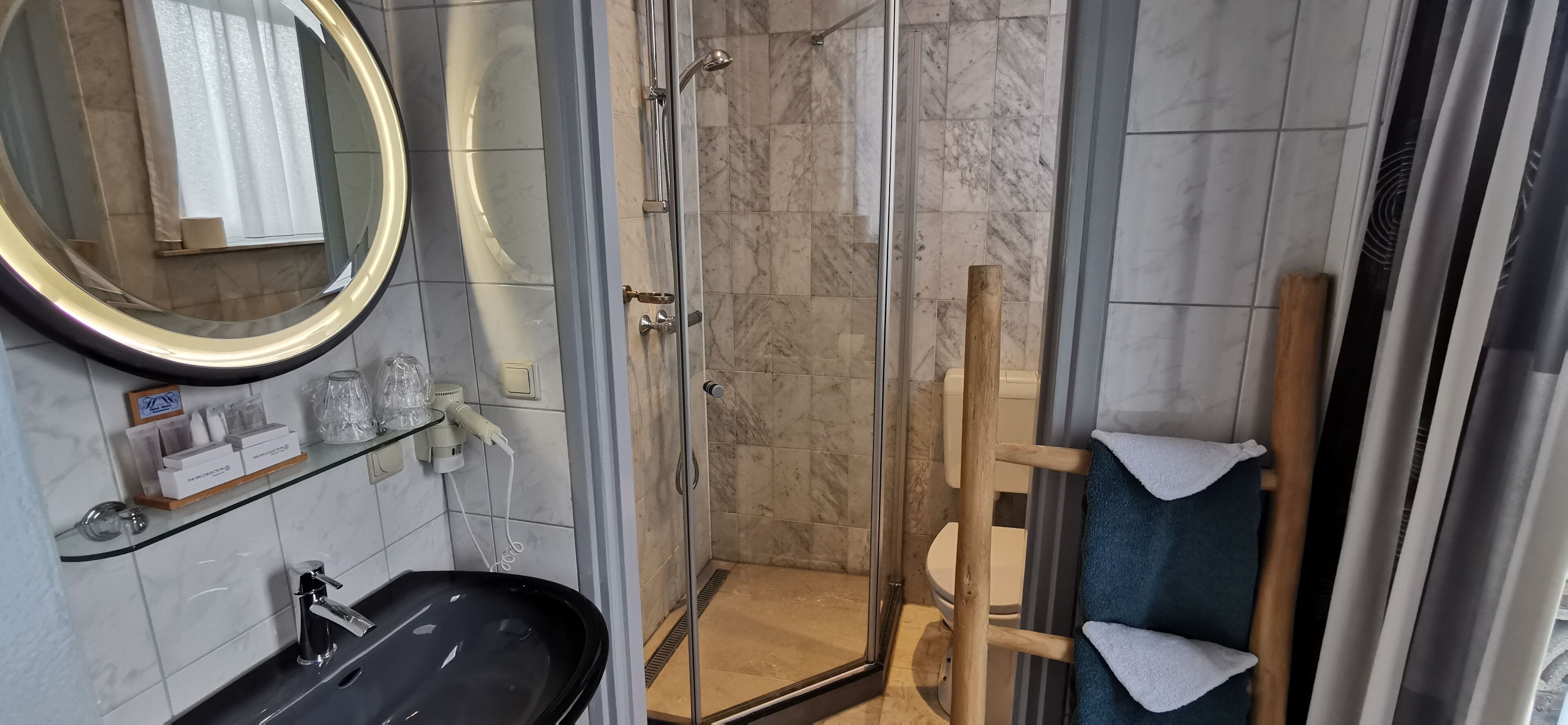 A modern bathroom with a glass-enclosed shower, a black sink, a large mirror, and a wooden towel rack.