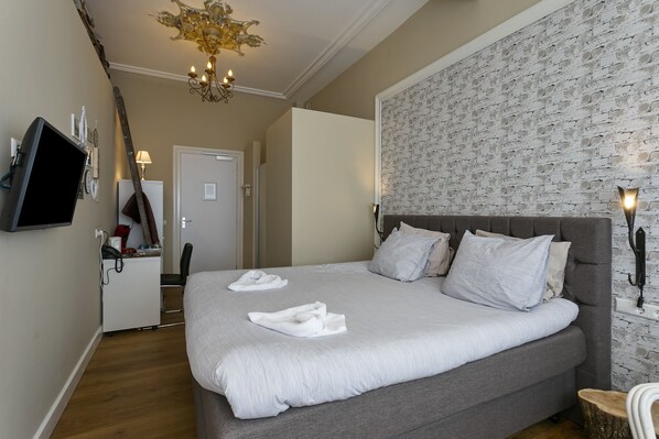 A neatly made bed with white linens and towels, a modern chandelier, and a brick-patterned wall. - Hotel Heere (Raamsdonksveer)