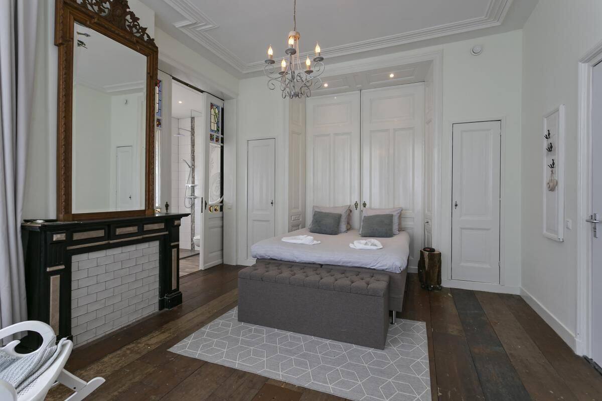 A bedroom with a large bed, a chest of drawers, a mirror, and a chandelier.