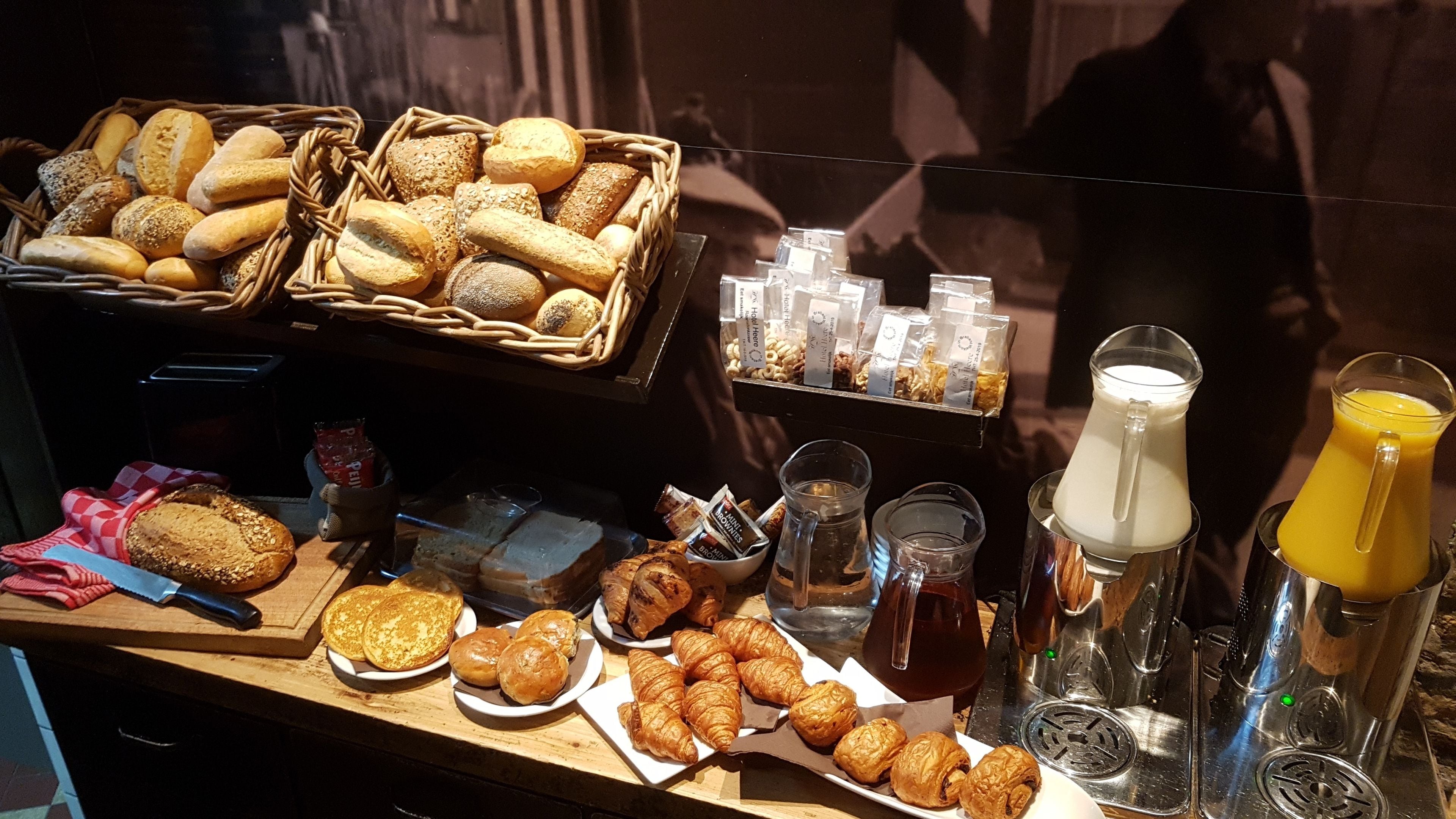 A breakfast buffet with various breads, pastries, and beverages.