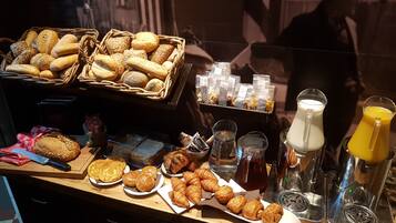 A breakfast buffet with various breads, pastries, and beverages.