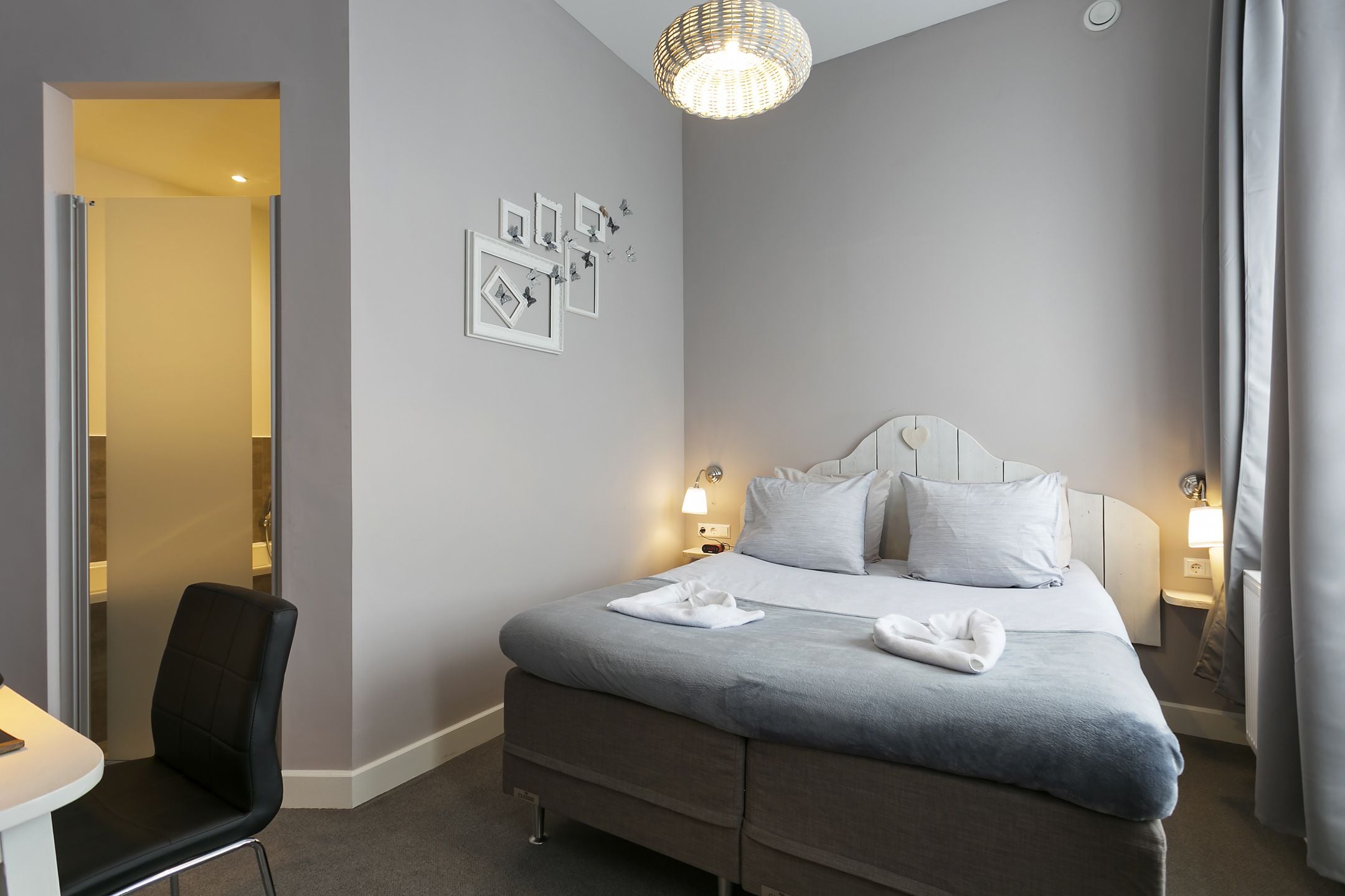 A neatly arranged hotel room with a bed, bedside tables, a desk, and a chair.