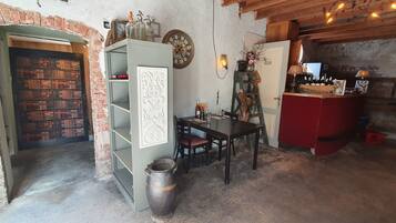Een eenvoudige kamer met een bakstenen muur, een houten tafel met stoelen, een boekenkast, een rode kast en een decoratieve klok.
