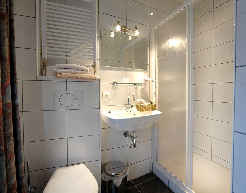 A bathroom with a white sink, mirror, and toilet. There is a towel rack above the sink and a shower curtain to the right.