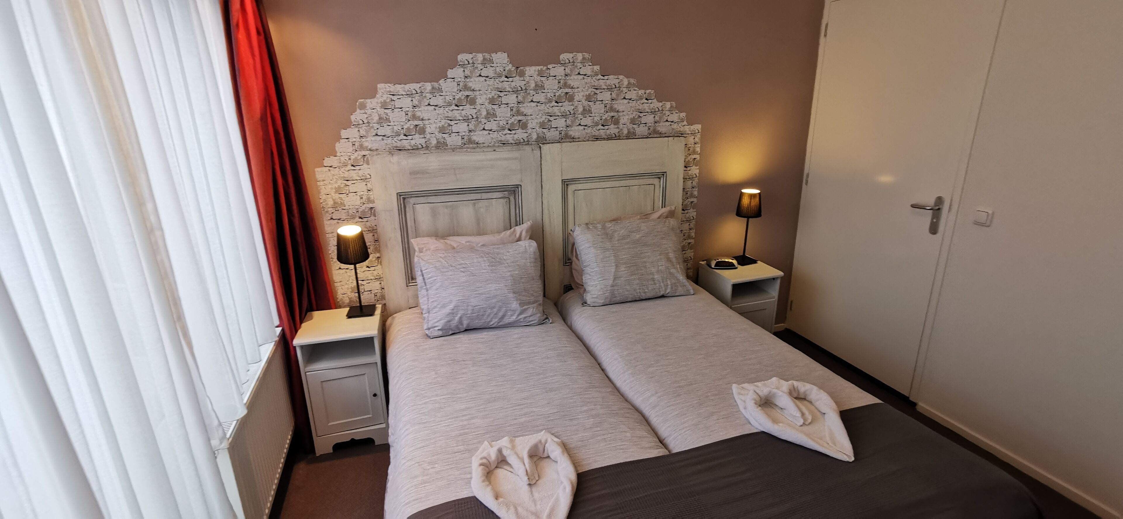 Een tweepersoonsbed met twee kussens, een nachtkastje met een lamp en een kledingkast.