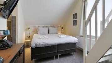 A bedroom with a bed, bedside lamps, a desk with a telephone, and a window with curtains.