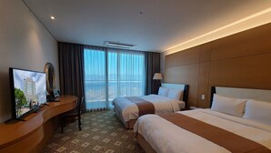 Une chambre d’hôtel avec deux lits, un bureau avec une télévision et une vue sur la ville grâce à de grandes fenêtres.