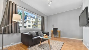 A modern living room with a sofa, a small round table, a floor lamp, and a TV mounted on the wall. - Forenom Serviced Apartments Oslo Rosenborg (Oslo)