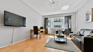 A modern living room with a flat-screen TV mounted on the wall, a black leather sofa, a round coffee table, and a dining area with a wooden table and chairs. - Forenom Serviced Apartments Oslo Rosenborg (Oslo)