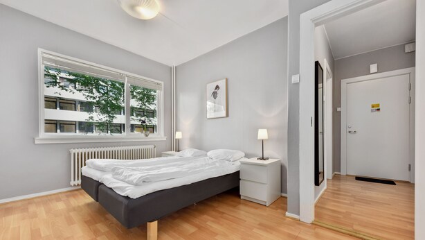 A modern bedroom with a large window, a bed, bedside tables, and a door. - Forenom Serviced Apartments Oslo Rosenborg (Oslo)